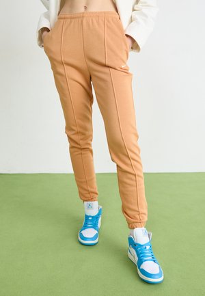 Pantaloni jogger beige con elastico in vita, tasche laterali e cuciture a contrasto; abbinati a sneakers alte blu e bianche.
