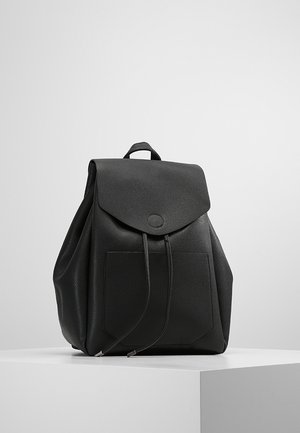 Černý kožený batoh s klopovým zavíráním, přední kapsou, šňůrkovými stahováními a horním madlem, odpočívající na bílém podstavci na jednobarevném pozadí.