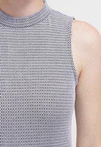 Bez rękawów top z kołnierzem w czarno-białym geometrycznym wzorze, wykonany z teksturowanej dzianiny i dopasowanej sylwetki.