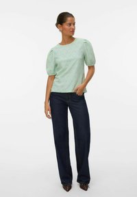 Blusa verde menta con maniche a sbuffo, caratterizzata da un motivo a diamante. Abbinata a pantaloni a gamba larga in denim scuro e scarpe marroni a punta.