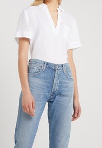 Chemise en lin blanche à manches courtes avec un col en V et une poche poitrine, associée à un jean taille haute bleu clair avec un délavage clair.