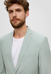 Błękitny marynarkowy żakiet z fakturowanej tkaniny, z jednolitą kieszenią na piersi i kołnierzem w stylu notch, nałożony na biały t-shirt.