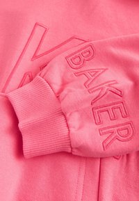 Rosa Sweatshirt-Ärmel mit Rippbündchen, mit erhabener, gestickter Schrift "BAKER" in passendem pinkfarbenem Garn.