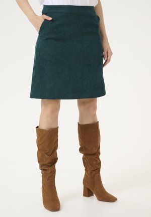 Spódnica z turkusowego sztruksu o prostym fasonie, z bocznymi kieszeniami i gładką fakturą, zestawiona z brązowymi, zamszowymi kozakami za kolano.