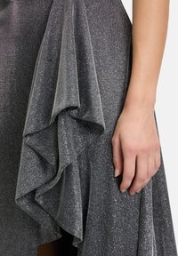 Silbernes Metallickleid mit strukturiertem Stoff, das Schichten von Rüschen aufweist und eine glatte Haptik hat, die einen zarten Schimmer hervorhebt.