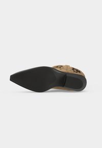 Vue de la semelle d'une botte de cow-boy beige avec une semelle extérieure en caoutchouc noir texturé et un talon sur fond blanc.