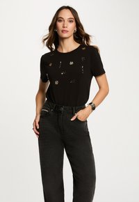Sort t-shirt med korte ærmer, pyntet med guld- og sølvudsmykninger. Kombineret med højtaljede sorte denimjeans.
