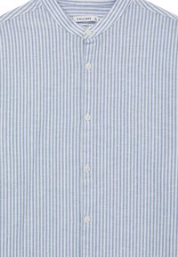 Camicia a righe blu chiaro e bianca con colletto alla cinese, dotata di una patta frontale con bottoni bianchi e un tessuto testurizzato.