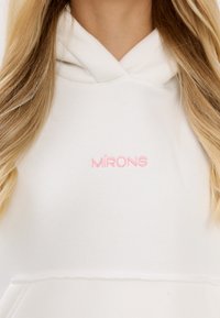 Witte hoodie met geborduurde tekst "MIRONS" in lichtroze. Bevat een voorzak en is gemaakt van een gestructureerde stof met een relaxte pasvorm.