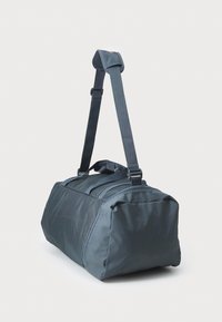 Grå duffel taske med justerbar rem og top-håndtag, har en rektangulær form, holdbart stof og lynlåslommer.