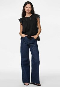 Top nero senza maniche con spalle arricciate, caratterizzato da un design arricciato e dettagli in pizzo. Abbinato a jeans blu in denim a gamba larga con vita alta.