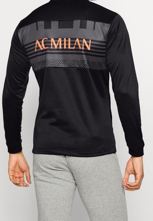 Chemise noire à manches longues avec un panneau gris présentant un motif texturé. "AC MILAN" en orange sur le haut du dos. Tissu lisse.