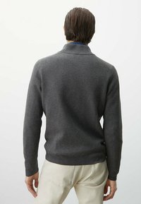 Grauer Strickpullover mit strukturiertem Muster, ausgestattet mit Kragen und eng anliegenden Bündchen, kombiniert mit hellen Hosen.