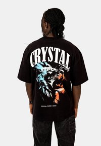 Černé volné tričko s velkým potiskem barevného lva a textem "CRYSTAL PARIS" na zádech. Volný střih, krátké rukávy.
