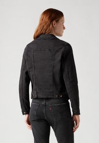Giacca in denim nero con un design aderente, chiusura frontale con bottoni e due tasche posteriori. Tessuto liscio, colletto classico e dettagli di cucitura a contrasto.
