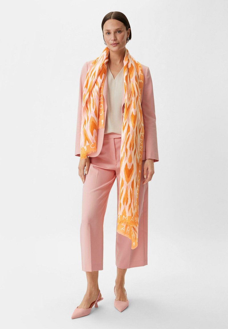 Pomarańczowy i różowy szalik w wzory wykonany z lekkiego materiału, noszony z jasną bluzką i różowym garniturem, z wyciętymi spodniami i szpilkami.