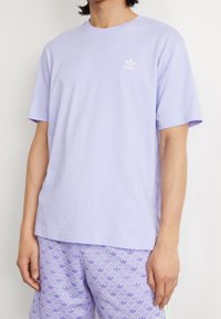 Světle fialové bavlněné tričko s krátkým rukávem a kulatým výstřihem. Na levé hrudi je vytištěno malé bílé logo Adidas.