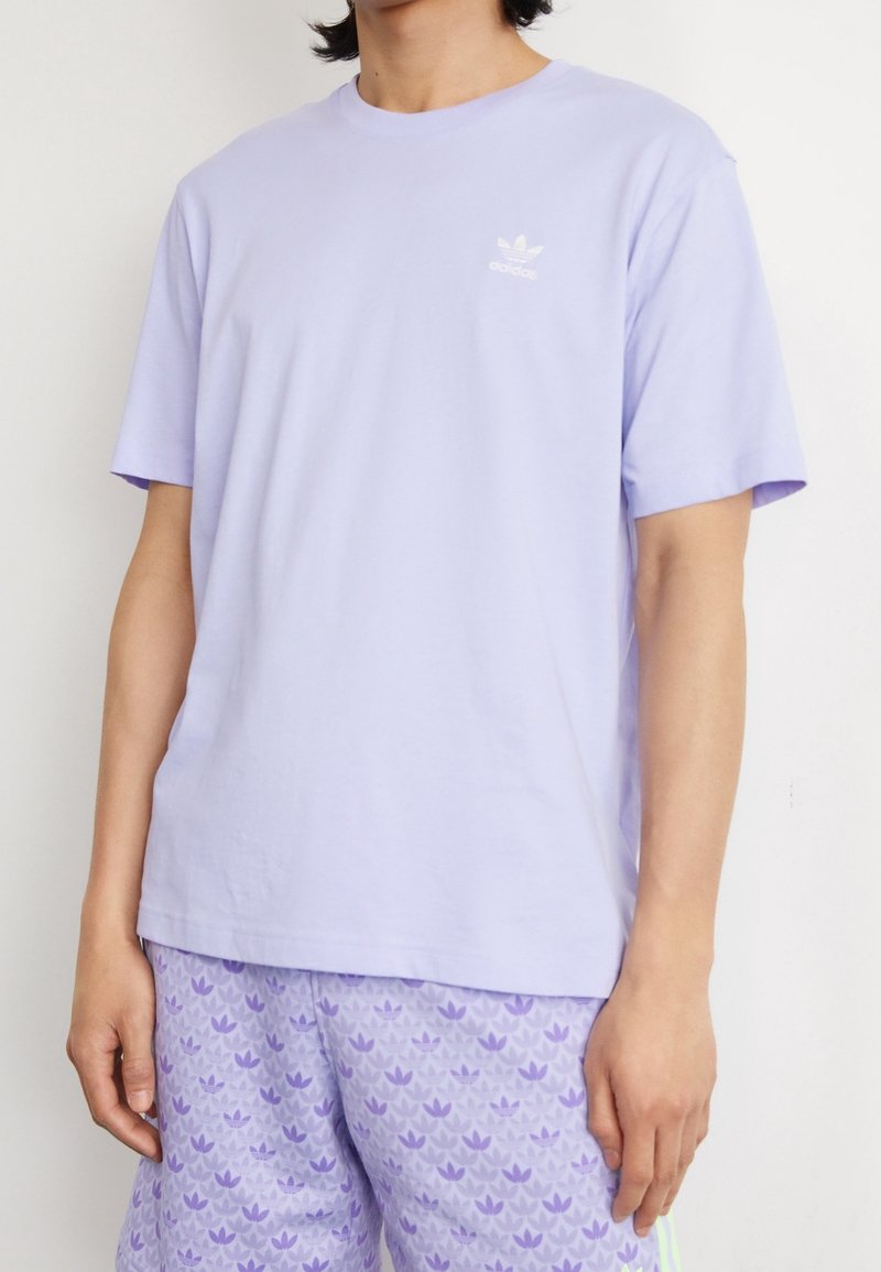 Světle fialové bavlněné tričko s krátkým rukávem a kulatým výstřihem. Na levé hrudi je vytištěno malé bílé logo Adidas.