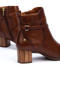 Brown leather ankle boots with a ribbed design, a side zipper, a gold buckle accent, and a stacked wooden heel.