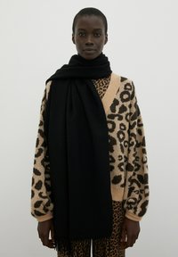 Leopardenmuster-Pullover in Beige und Schwarz, kombiniert mit einem langen schwarzen Schal. Beide Kleidungsstücke zeichnen sich durch weiche Texturen und lockere Passformen aus.