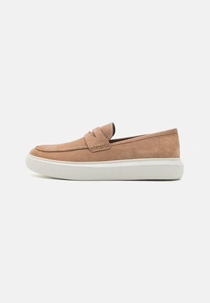Mocassini in suede marrone chiaro con suola bianca piatta. Presentano un design cucito sottile e uno stile slip-on minimalista.
