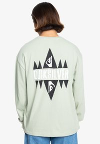 Light green long-sleeve shirt with a large black and white geometric graphic on the back, featuring the word "QUIKSILVER." Soft cotton material.