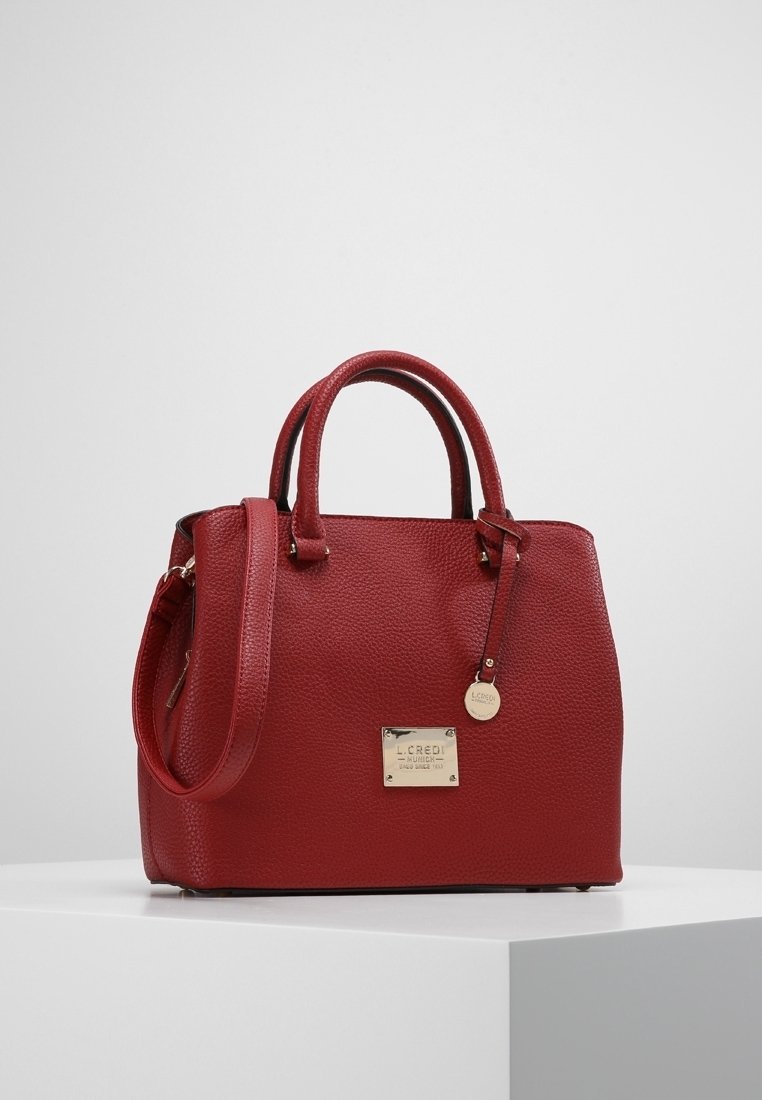 Röd läderhandväska med en strukturerad yta, dubbla handtag i toppen och en justerbar axelrem. Har en metallisk varumärkesplatta.