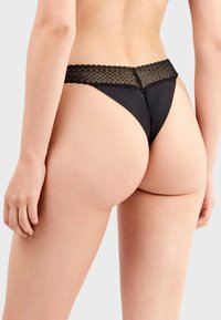 Tanga negro con cinturilla de encaje, textura de tela suave y diseño de cobertura mínima.