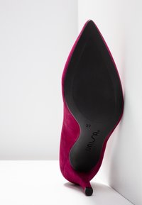 Chaussure à talon haut en daim rose à bout pointu, posée sur le talon, montrant la semelle noire avec la taille 37 et la marque Unisa.