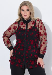 Blusa nera trasparente con ricami floreali rossi, accenti in pizzo, chiusura a bottoni e maniche lunghe. Presenta un colletto classico e una silhouette aderente.