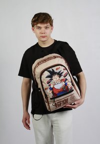 Sac à dos beige avec un graphique d'un personnage aux cheveux noirs. Inclut plusieurs compartiments, des accents noirs et des illustrations de nourriture.