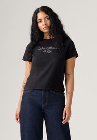 Svart T-skjorte med kort erm laget av bomull, med brodert "Levi Strauss & Co." logo på forsiden, sammen med mørke denimbukser.