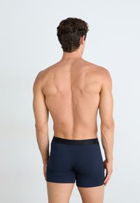 Boxer shorts bleu marine en tissu lisse, avec une ceinture élastique noire, présentés de dos. Design à jambes courtes, détails minimaux.