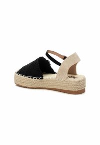 Sandal espadrille negra y beige con parte superior trenzada, correa ajustable en el tobillo y una entresuela de cuerda de yute. Suela plana de goma marrón.
