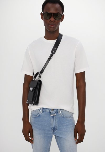 Weißes T-Shirt mit kurzen Ärmeln; hellblaue Jeans; schwarze Leder-Umhängetasche mit silberner Beschläge; runde Sonnenbrille mit dunklen Gläsern.