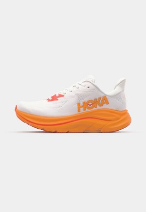Scarpa da corsa bianca con imbottitura arancione e dettagli rossi. Presenta una parte superiore in rete, logo sul lato e una suola spessa e testurizzata.