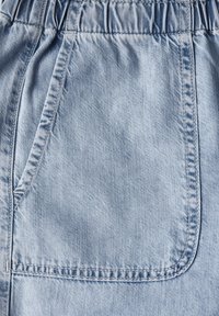 Hellblauer Denim-Stoff mit einem elastischen Bund und einer seitlichen Tasche mit sichtbaren Nähdetails. Weiche Textur, lässiges Design.