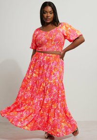 Ensemble floral deux pièces comprenant un top court froncé et une jupe maxi à volants. Les couleurs incluent le rose, l'orange et des nuances de jaune. Tissu léger.