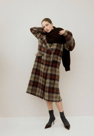 Manteau à carreaux en mélange de laine aux tons crème, marron et bleu ; design croisé avec de larges revers. Porté avec une écharpe sombre et des talons pointus.