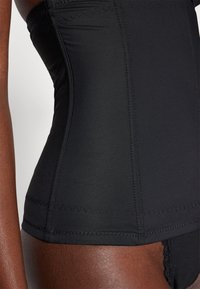 Black corset-style garment, featuring smooth fabric, structured design, and zigzag stitching along the edges. No visible patterns or hardware.
