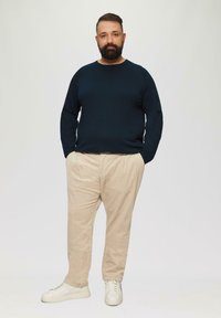 Navy gestrickter Pullover, beige Cordhose und weiße Sneakers. Gerader Schnitt; weiche Textur; Outfit geeignet für Freizeitkleidung.