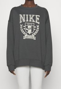 Mörkgrå oversized sweatshirt med en vintage-stil vit Nike-logotyp och en skölddesign med texten "1972" och "Oregon". Mjuk tyg.