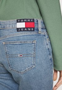 Vaaleansiniset farkut suoran lahkeiden leikkauksella. Vyötäröllä on musta, punainen ja valkoinen brändiläppä sekä pieni logo takataskussa.