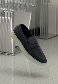 Scarpe slip-on in pelle blu navy con punta arrotondata, dotate di una fascia decorativa e una suola in gomma traslucida. Logo discreto sul lato.