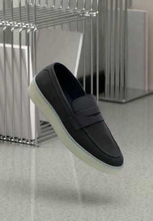 Scarpe slip-on in pelle blu navy con punta arrotondata, dotate di una fascia decorativa e una suola in gomma traslucida. Logo discreto sul lato.