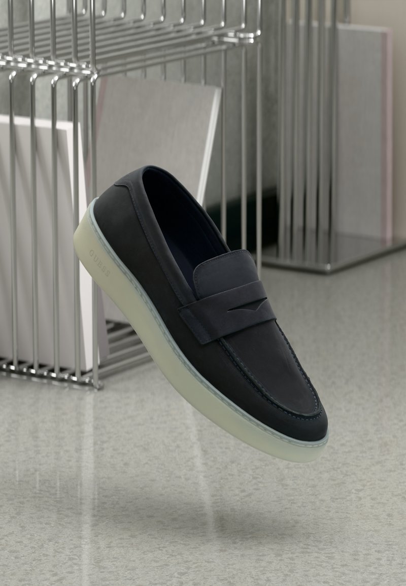 Scarpe slip-on in pelle blu navy con punta arrotondata, dotate di una fascia decorativa e una suola in gomma traslucida. Logo discreto sul lato.