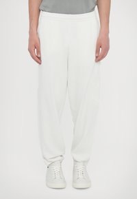 Hvide sweatpants med elastisk talje, tætsiddende ben og en blød tekstur. Har et diskret logo detaljeret på siden. Sæt det sammen med hvide sneakers.