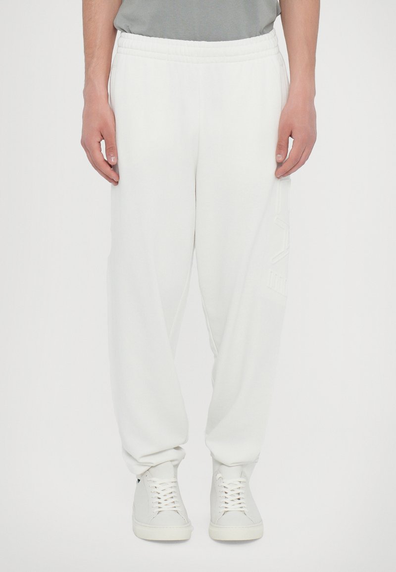 Hvide sweatpants med elastisk talje, tætsiddende ben og en blød tekstur. Har et diskret logo detaljeret på siden. Sæt det sammen med hvide sneakers.