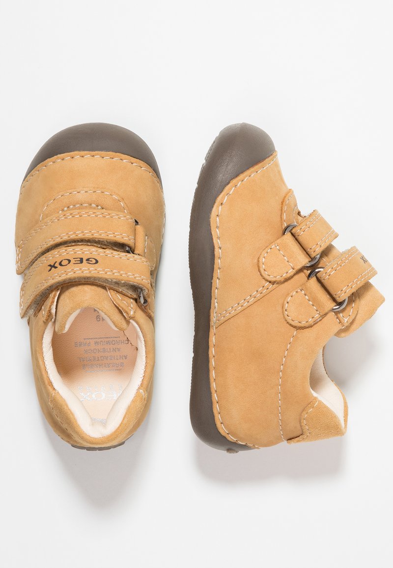 Scarpe per bambini in pelle color cuoio con suole in gomma marrone, doppie cinghie con chiusura a strappo e dettagli in cucitura bianca. Design con punta arrotondata.