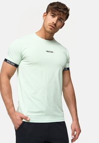 Camiseta verde menta clara hecha de una tela suave, con detalles en negro en las manga y un logotipo centrado en una fuente minimalista.